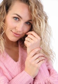 Gouden en zilveren ringen met delicate ontwerpen gedragen aan vingers. Het model draagt een zachtroze, gestructureerde trui met een V-hals.