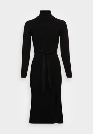Zwarte midi-jurk met lange mouwen en coltrui, stoffen ceintuur geknoopt aan de taille en voorste split op een effen lichte achtergrond.