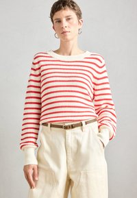Maglione a righe rosse e bianche in maglia con texture a coste, scollatura rotonda e spalle scese, abbinato a pantaloni beige a vita alta.