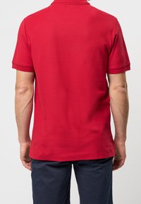 Czerwona koszulka polo z krótkimi rękawami, prążkowanym kołnierzykiem i gładką fakturą. Zaprojektowana z myślą o komforcie, z prostym dołem i minimalnymi detalami.