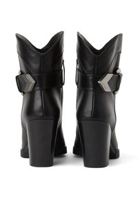 Črne usnjene gležnjarje s koničastim dizajnom, ki imajo širok rob, stransko zaponko in debel petek. Gladka tekstura in sijoč zaključek.