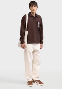 Brun långärmad pikétröja med bröstficka, krämfärgade vida byxor och bruna sneakers med vita ränder. Tyget ser mjukt ut.