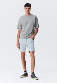 Gray short-sleeve t-shirt paired with light blue denim shorts. The model wears black high-top shoes with white soles, hands in pockets.