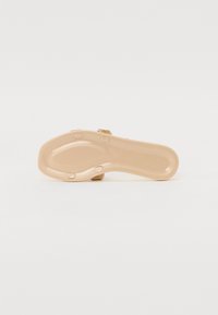 Beige sandaalipohja, jossa on uritettu pinta, pyöreät pitoakcentit ja hienovaraiset kimalteleva hihnaviimeistely. Litteä, ergonominen muotoilu.
