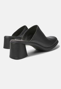 Zwarte leren muleschoenen met brede blokhakken en open achterkant, weergegeven vanuit een schuine achteraanzicht op een witte achtergrond.