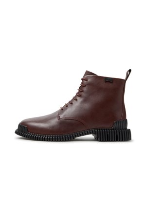 Brauner Leder-Stiefel mit Schnürung vorne und schwarzer strukturierter Sohle, mit kleinem Zuglasche an der Ferse und einem Markenlabel nahe dem oberen Teil.