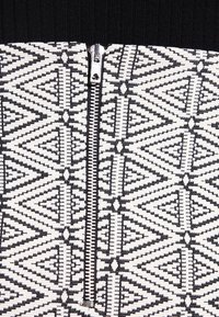 Gros plan d'un tissu à motif géométrique noir et blanc avec une fermeture éclair argentée au centre sur un fond noir.