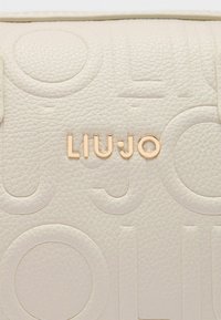 Borsa in pelle testurizzata color crema con motivi circolari in rilievo e logo dorato "LIU•JO" sul fronte.