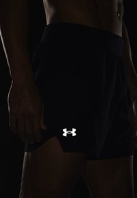 Pantalones cortos deportivos negros hechos de material ligero, con un logo blanco en la parte inferior derecha y un diseño texturizado sutil.