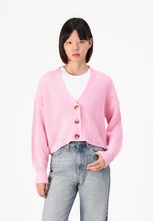 Cardigan rosa lavorato a maglia con scollatura a V, tre grandi bottoni e maniche ampie, abbinato a jeans azzurri chiari con motivi a stelle.