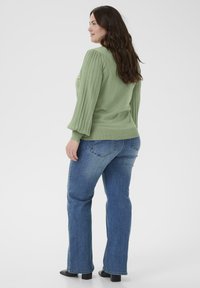 Lysegrøn ribstrikket sweater med puffede ærmer, kombineret med blå vidde jeans og sorte blokhælede støvler, set bagfra.