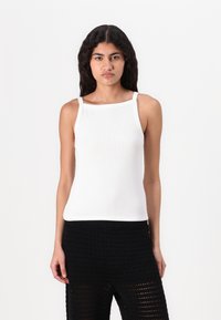 Top de tirantes blanco con textura y escote cuadrado, combinado con pantalones de punto negro texturizados.