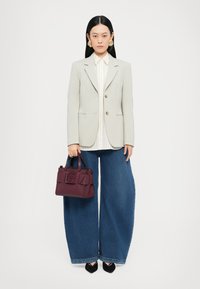 Blazer gris clair avec boutons dorés, chemise blanche rayée, jeans bleu à jambes larges et petit sac bordeaux avec des détails texturés. Chaussures noires.