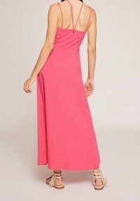 Dlouhé růžové šaty s tenkými ramínky, přiléhavým korzetem a A-linií. Mají malý knoflíkový uzávěr na zadní straně a hladkou texturu látky.