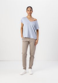 T-shirt azzurro chiaro a spalle scoperte, vestibilità ampia, abbinato a pantaloni beige a vestibilità slim e sneakers bianche; tessuto morbido, design informale.