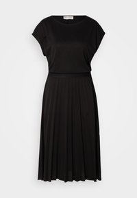 Musta mekko, jossa on rento yläosa lyhyillä hihoilla, istuva vyötärö ja laskostettu, virtaava hame. Sujuva ja pehmeä kankaan rakenne.