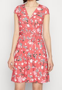 Robe portefeuille corail à motifs floraux. Manches courtes, encolure en V et taille nouée. Présente des détails de fleurs roses, bleues et noires.