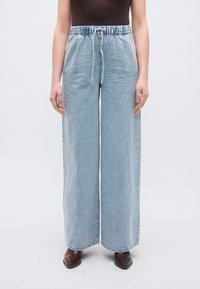 Φαρδιά τζιν παντελόνια από τζιν ύφασμα σε ανοιχτό γαλάζιο χρώμα, με ελαστική μέση, ρυθμιζόμενο κορδόνι και casual, χαλαρή εφαρμογή.