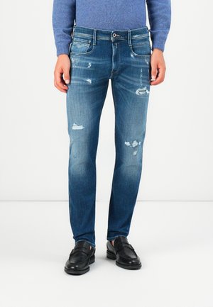 Heren versleten blauwe jeans gemaakt van denim, met een slim fit, scheuren en een vervaagde afwerking. Gecombineerd met zwarte instappers.