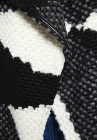 Tessuto lavorato a maglia bianco e nero con un motivo testurizzato; presenta una zip nera lucida. Il design include forme a blocchi a contrasto.