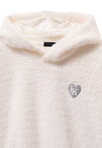 Weißer, flauschiger Kapuzenpullover mit einem kleinen silbernen Herzemblem und den Initialen "IK" auf der Brust.