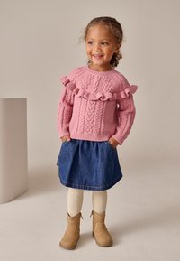 Pulover tricotat roz cu detalii de volane, combinat cu o fustă din denim, ciorapi texturați crem și bocanci maro până la gleznă.
