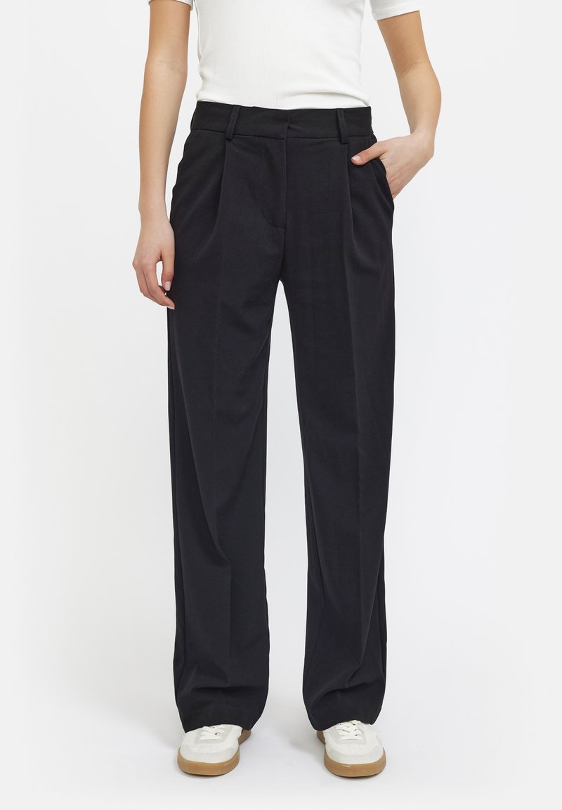 Zwarte wijde broek met plooien, gemaakt van een gladde stof, met zijzakken en een klassieke tailleontwerp. Gecombineerd met witte sneakers.