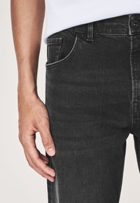 Czarne dżinsy z denimu o dopasowanym kroju, subtelnej fakturze, z pięcioma kieszeniami i zapinane na guzik w talii.