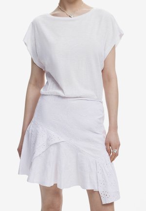 Woman wearing a white short-sleeve top and a textured white A-line skirt with eyelet details, accessorized with silver necklace and ring.