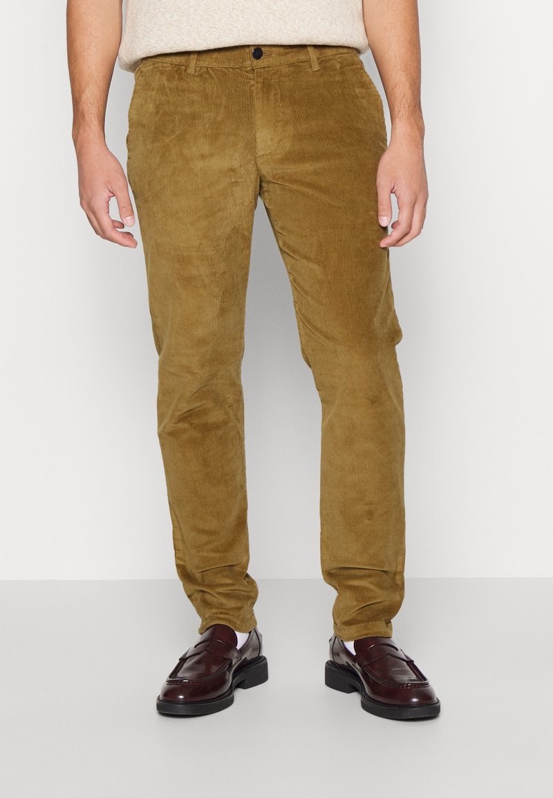 Kaki corduroy broek met een zachte textuur, een slanke pasvorm en steekzakken aan de voorkant, gecombineerd met donkerbruine loafers voor een complete look.