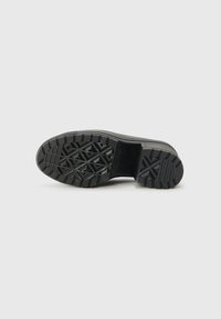 Semelle en caoutchouc noir de basket avec un motif de tressage en diamant, talon plat, forme arrondie et texture lisse. Logo embossé sur le côté.