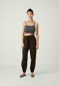 Sivor skrajni top, olivno zeleni tapered hlače z elastičnimi manšetami in svetlorjavi balerinki; minimalni dodatki, splošen casual videz.