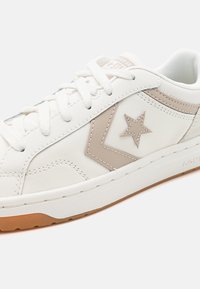 Sneaker en cuir blanc avec étoile beige et design en chevrons, avec des lacets blancs et une semelle en caoutchouc naturel, vu de côté.