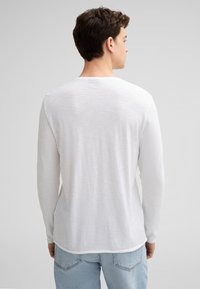 Langärmliges weißes Hemd aus leichtem, strukturiertem Material mit Rundhalsausschnitt, das einen lässigen Schnitt und dezente Details auf der Rückseite aufweist.