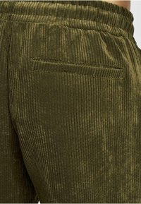 Pantalones de pana verde oliva con estrías verticales, con cinturilla elástica y un único bolsillo trasero. Textura suave, diseño casual.