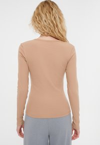 Dlouhý rukáv, přiléhavý top z jemného žebrovaného materiálu. Barva je taupe a má kulatý výstřih. V kombinaci se světle šedými kalhotami.