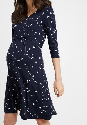Granatowa sukienka ciążowa z rękawami do połowy przedramienia, z dopasowaną górą, wiązaniem w talii oraz białym nadrukiem w ptaki na całej powierzchni.