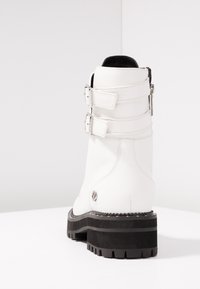 Botín de cuero blanco hasta el tobillo con dos correas ajustables, un tacón reforzado y una suela de goma negra gruesa con un patrón estriado.