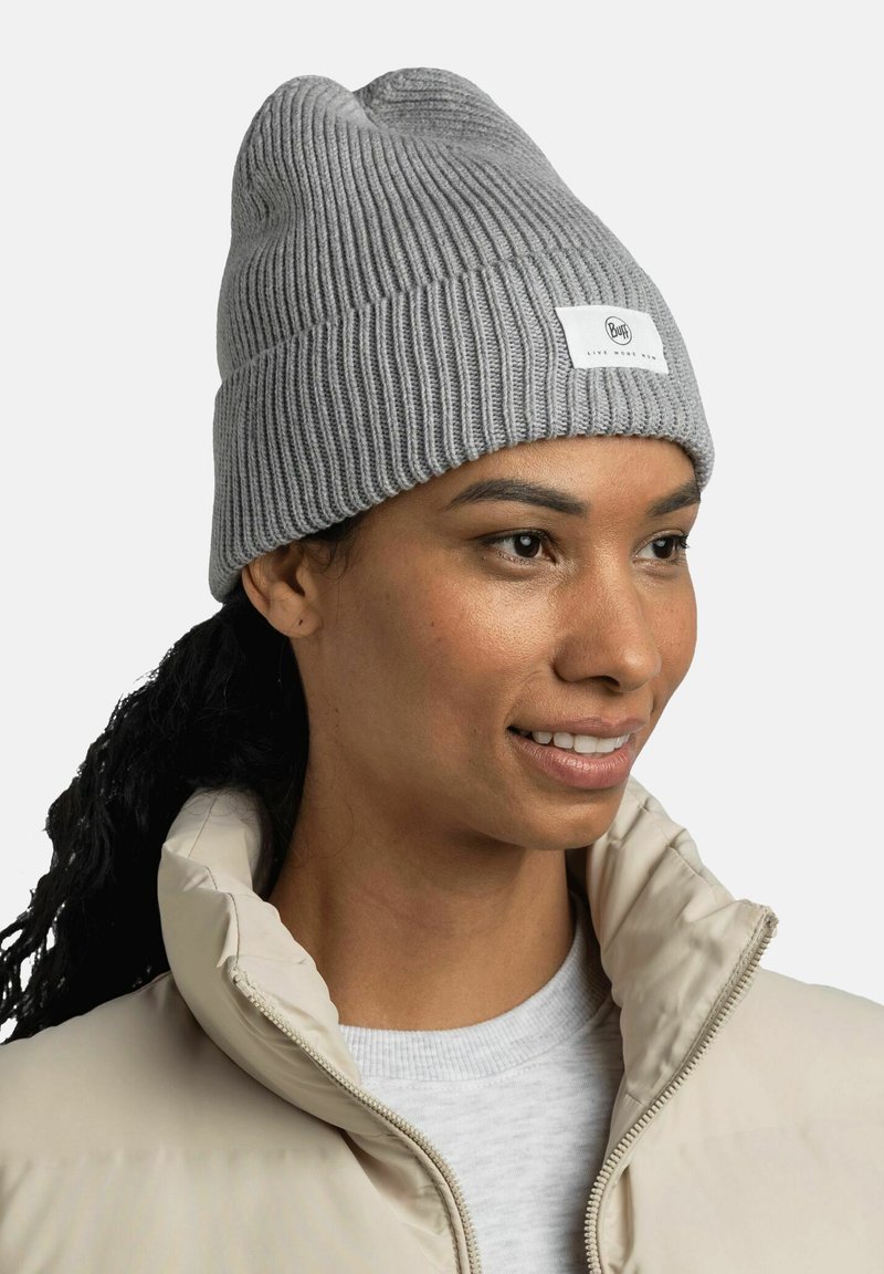 Gorro de lana gris con una textura acanalada y un dobladillo doblado, que presenta una pequeña etiqueta blanca. Llevado con una chaqueta de plumas beige.