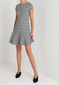 Robe à carreaux noir et blanc avec un corsage ajusté, des manches courtes et un ourlet évasé. Associée à des chaussures à talons hauts noires.