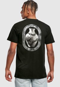Black cotton t-shirt featuring a large gray graphic on the back of an ornate vase with chains and a star design. Casual fit.