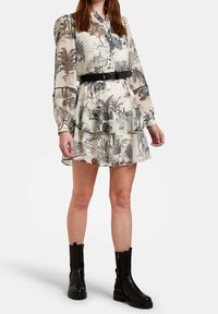 Šaty s květinovým vzorem a dlouhými rukávy, s volánkem na okrajích a páskem v oblasti pasu. Vyrobené z průhledné látky, převážně v krémové barvě s černými akcenty.