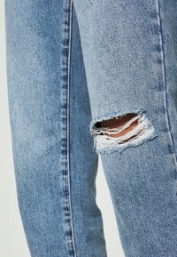 Ljusblå denimjeans med en sliten design, stora fransade knähål, lätt blekning och kontrasterande sömnad längs sidan.