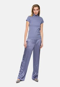 Hellblaue, enganliegende Rollkragenoberteil, kombiniert mit lockeren, schimmernden hellblauen Hosen. Die Hosen haben eine glatte Textur und Vorderfalten.