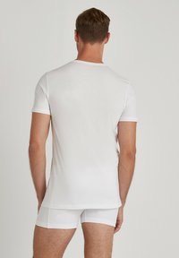 White cotton t-shirt with short sleeves and a round neck, paired with white shorts, displayed from the back against a neutral background.