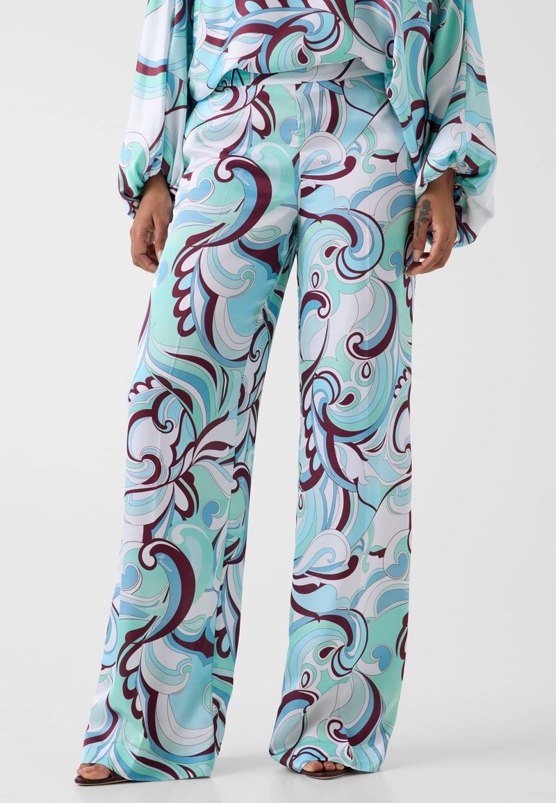 Pantalon à jambes larges avec des tourbillons abstraits fluides en bleu pétrole, blanc et bordeaux, porté avec un haut ample assorti et des sandales marron.