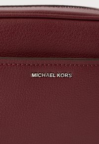 Bordowa skórzana torebka z fakturowaną powierzchnią i srebrnym logo "MICHAEL KORS". Elementy wyróżniające to staranne szwy wzdłuż szwów.
