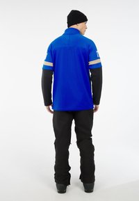 Blauwe polo met zwarte lange mouwen, heeft een stof van gaas, twee horizontale strepen in lichtblauw en beige, gecombineerd met zwarte broek en laarzen.