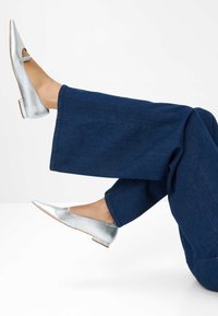 Zilveren metallic ballerina's met een spitse neus en uitsnijdingen aan de zijkant. Gecombineerd met donkerblauwe wide-leg jeans, met een nette zoom en een gladde textuur.
