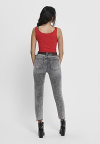 Red tank top, gray faded denim jeans with a high waist, front and back pockets, frayed hem, and black ankle boots. Belt visible.